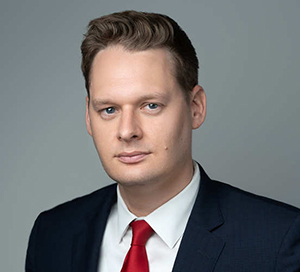 man with dark hair wearing business attire and a red tie